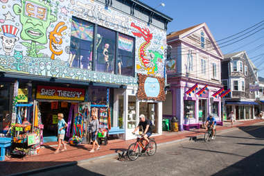 people biking and walking in front of colorful shops on a main street