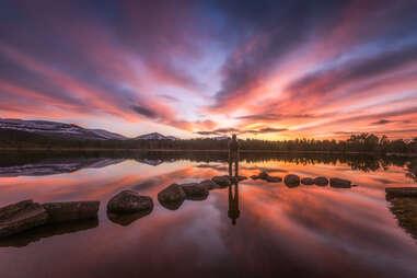 hiker standing on stone in cairngorms national park at sunset